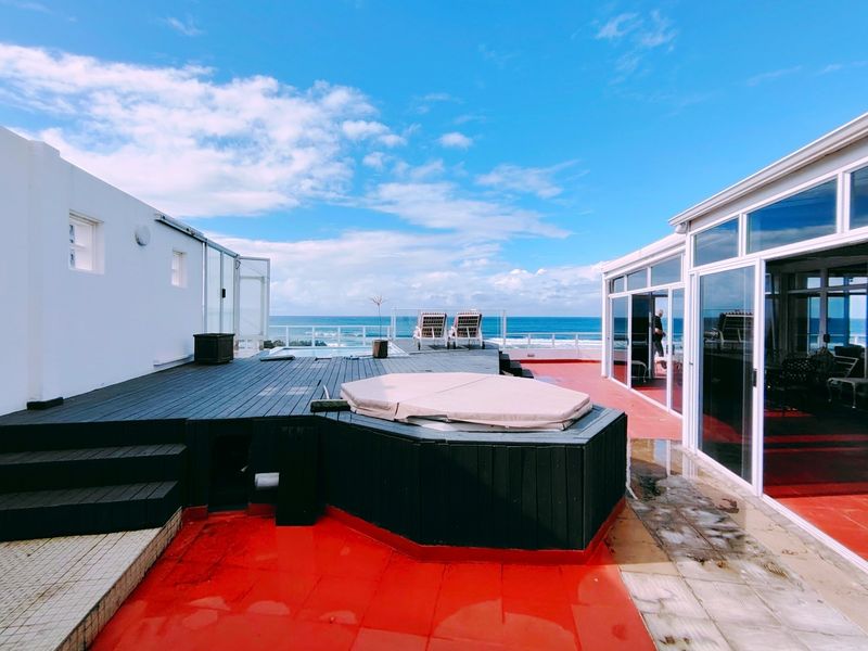 Spacious penthouse terrace featuring timber decking, a built-in spa, and panoramic ocean views, offering an ideal setting for outdoor entertainment.