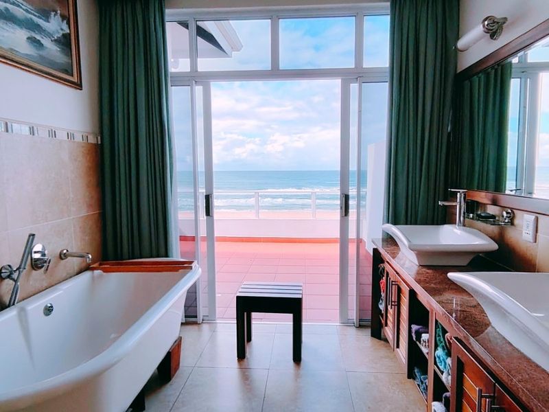 Spacious bathroom featuring a freestanding tub, double vanity with vessel sinks, and direct access to a private balcony with ocean views.