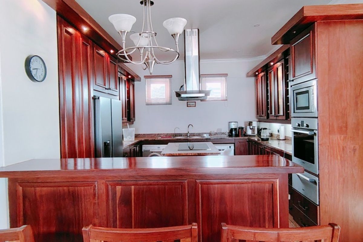 A well-appointed kitchen featuring rich wooden cabinetry, a central island with a breakfast bar, built-in appliances, and modern recessed lighting.