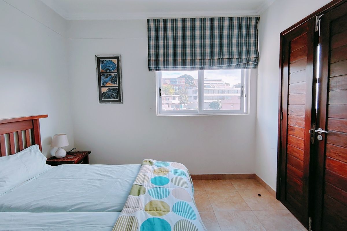 A bedroom featuring tiled flooring, a sliding window with a roman blind, and a solid wooden door.