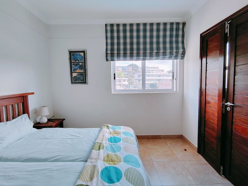 A bedroom featuring tiled flooring, a sliding window with a roman blind, and a solid wooden door.