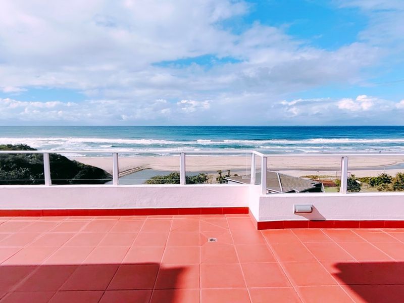 Spacious penthouse balcony featuring red tiled flooring and a modern glass balustrade, offering expansive, unobstructed ocean and coastal views.