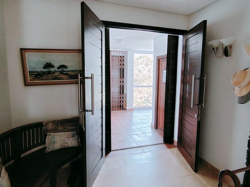 A welcoming entrance foyer featuring double wooden doors, tiled flooring, and a recessed ceiling design, leading through to an open balcony area.