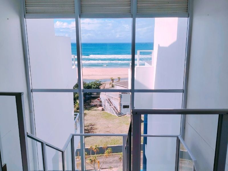 A bright hallway featuring a large floor-to-ceiling window with direct ocean views, tiled stairs, and modern metal railings.
