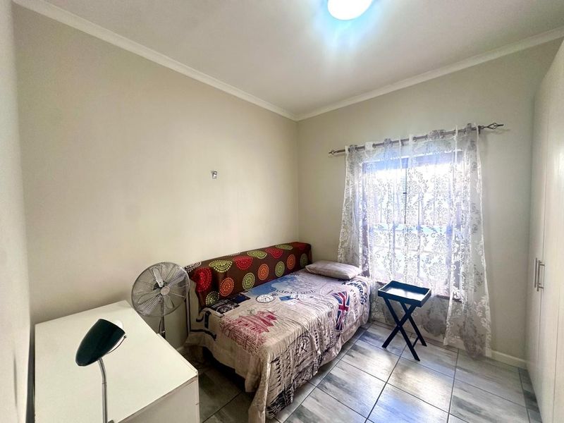 A compact bedroom featuring tiled flooring, a built-in wardrobe, and a window with a curtain rod.