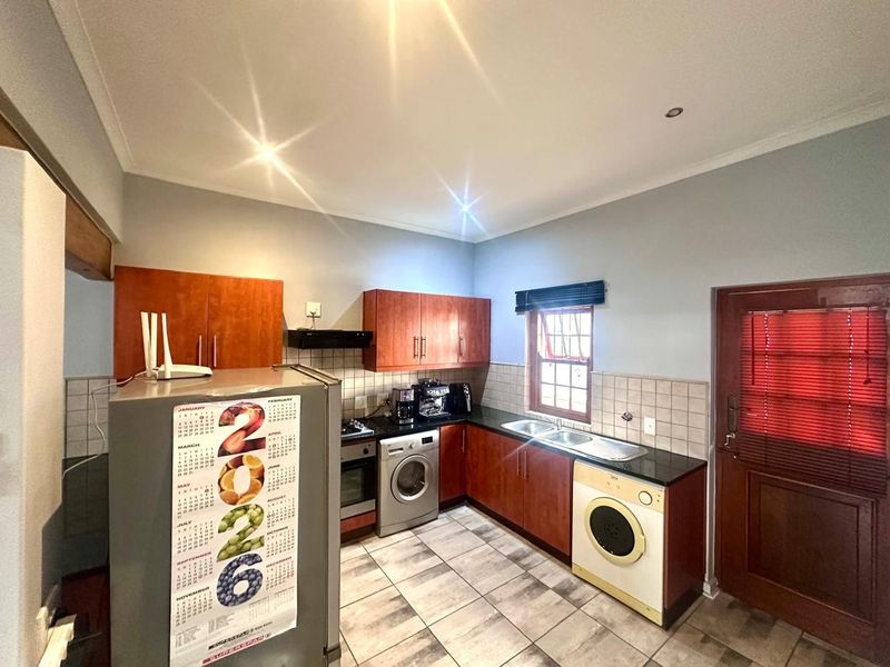 A functional kitchen featuring wooden cabinetry, dark countertops, tiled flooring, and integrated laundry appliances with direct access to an exterior door.