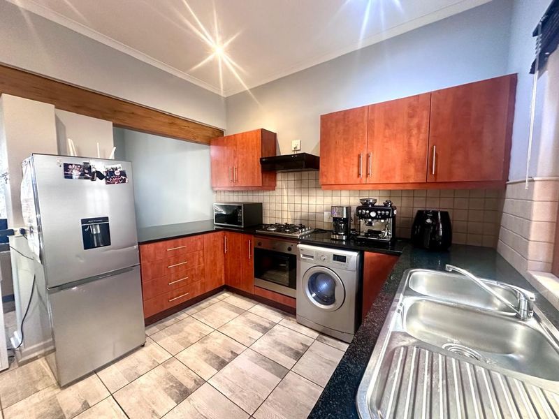 A functional kitchen featuring wooden cabinetry, granite countertops, a gas hob, built-in oven, and tiled flooring with a double sink.