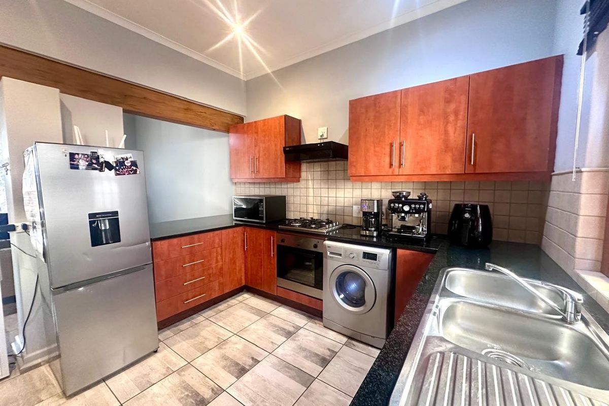 A functional kitchen featuring wooden cabinetry, granite countertops, a gas hob, built-in oven, and tiled flooring with a double sink.