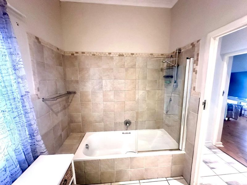 A functional bathroom featuring a built-in bathtub with a glass shower screen and neutral wall tiling.