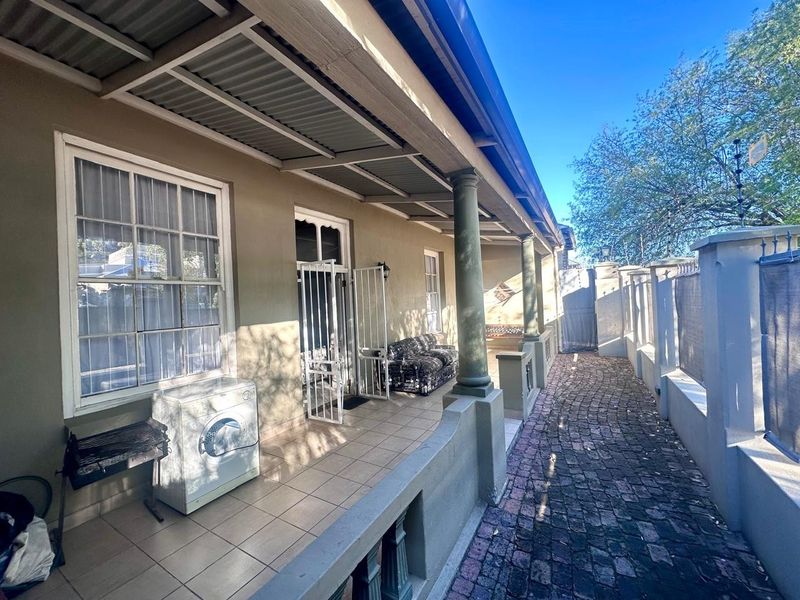 A covered patio area featuring tiled flooring, support columns, and direct access to the home, complemented by a cobblestone pathway along the side.