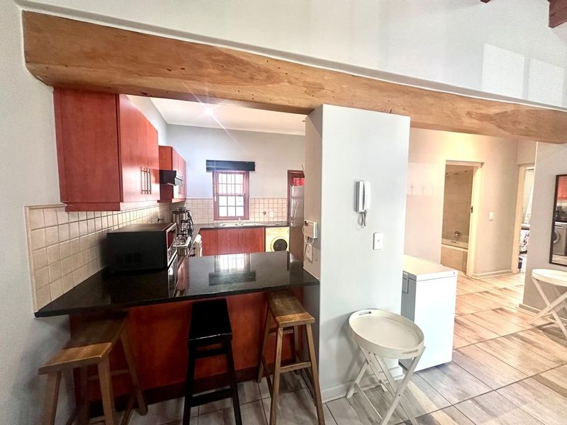 Open plan kitchen featuring wooden cabinetry, granite countertops, and a prominent exposed timber beam, with tiled flooring throughout the living area.