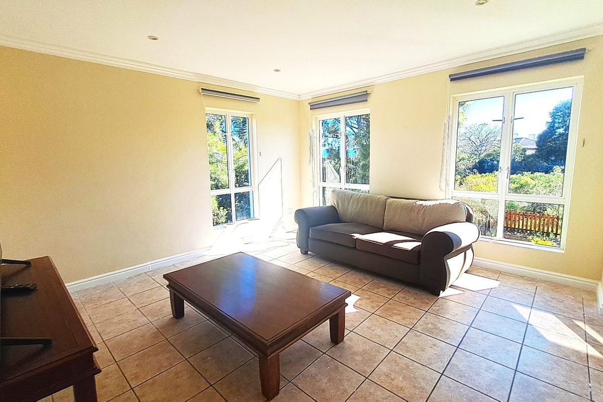 A bright living room featuring tiled flooring, recessed downlighting, and large windows that provide ample natural light and garden views.