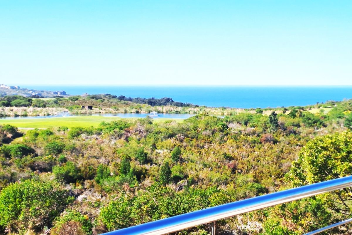 A scenic elevated view overlooking a natural landscape, pond, and the distant ocean, framed by a modern stainless steel balustrade.