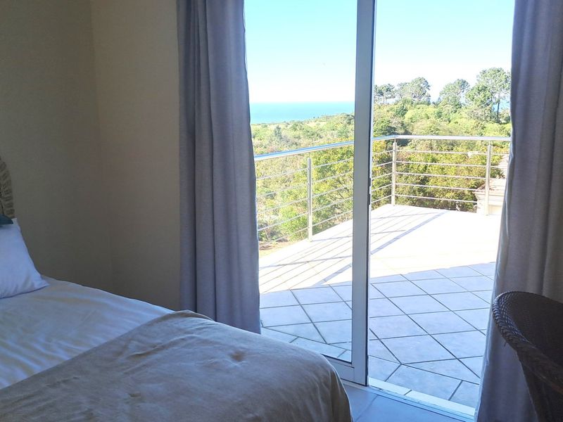 Bedroom featuring a sliding glass door that opens onto a tiled balcony with a stainless steel balustrade and scenic coastal views.