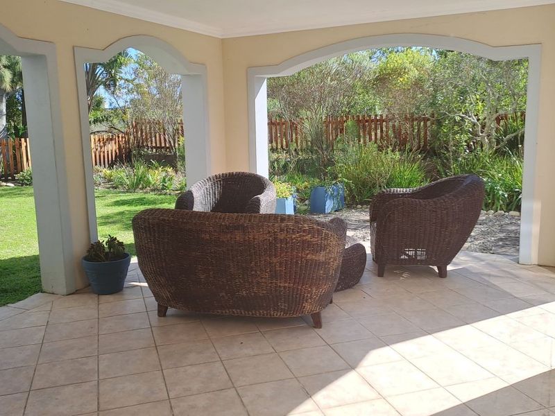 A covered patio area featuring tiled flooring and arched masonry pillars, overlooking a well-maintained garden with a wooden fence.