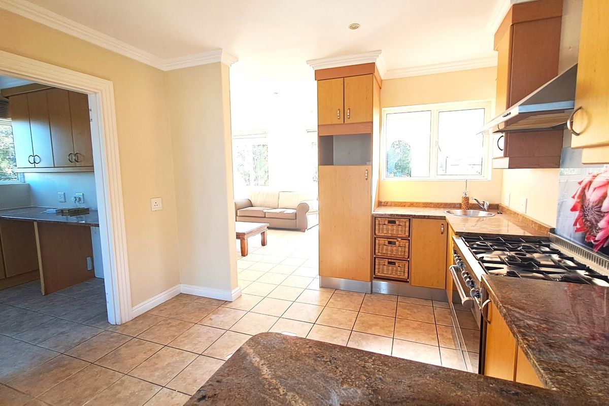 A functional kitchen featuring wooden cabinetry, stone countertops, a gas hob with extractor, and tiled flooring, with an adjacent scullery and open-plan living area.