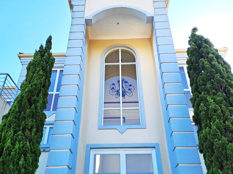 Front elevation of a multi-story residence featuring a prominent arched window, decorative blue quoins, and balcony railings.