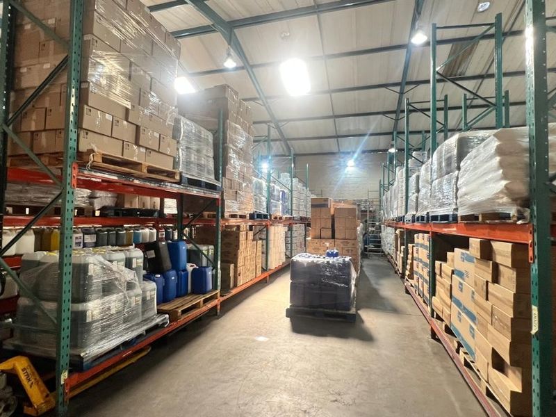 Spacious industrial warehouse featuring high-bay lighting, exposed steel roof trusses, durable concrete flooring, and extensive heavy-duty steel racking systems for storage.
