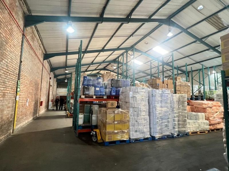 Spacious industrial warehouse featuring exposed brick walls, high steel truss ceilings, and extensive pallet racking for storage.