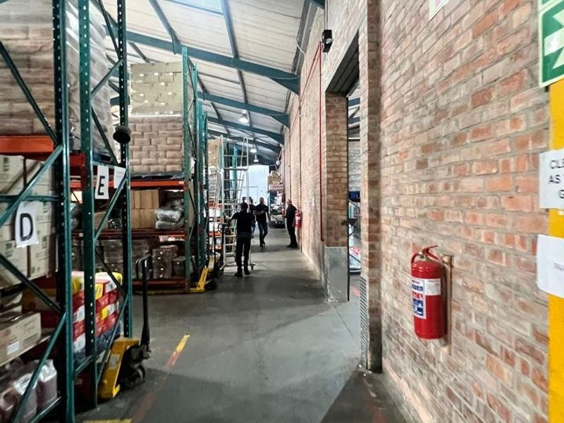 Industrial warehouse space featuring exposed brick walls, concrete flooring, high-level steel racking, and functional industrial lighting.