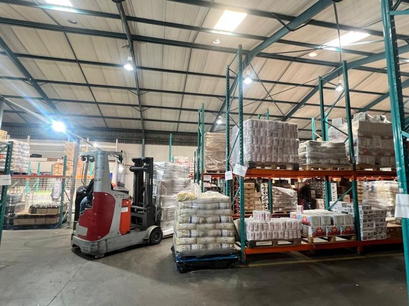 Spacious industrial warehouse facility featuring high-bay lighting, exposed steel roof trusses, and extensive heavy-duty racking systems for efficient storage and logistics operations.