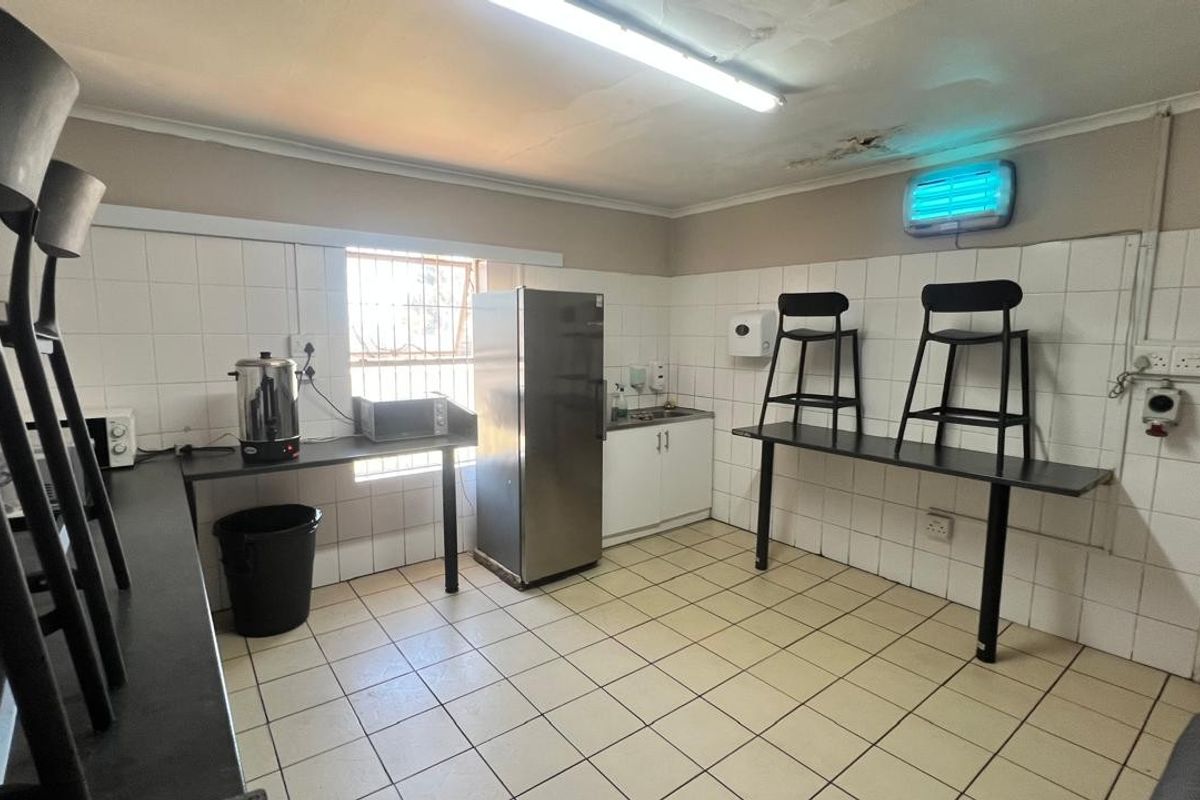A functional industrial kitchen area featuring tiled walls, tiled flooring, built-in cabinetry with a sink, and security bars on the window.
