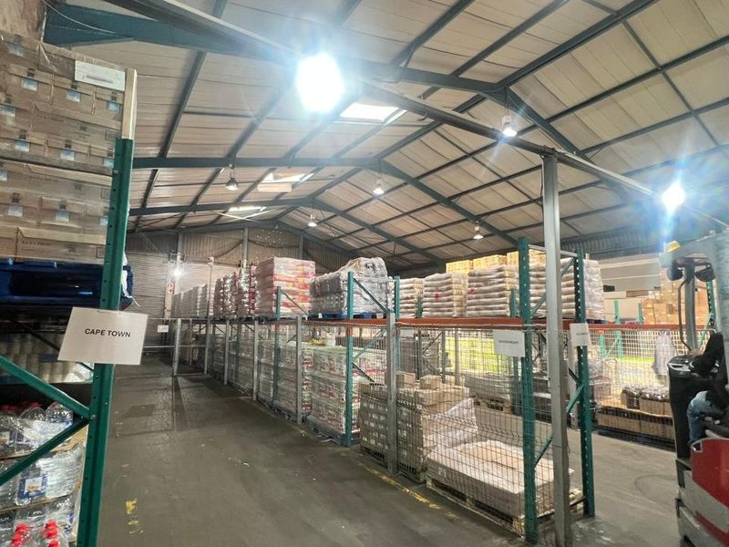 Spacious industrial warehouse facility featuring high-bay lighting, exposed steel roof trusses, and extensive heavy-duty steel racking systems for storage.