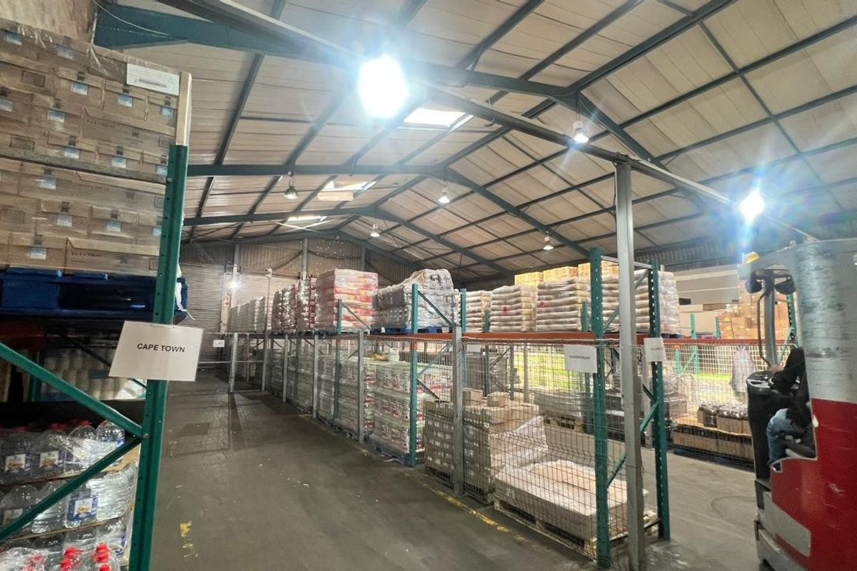 Spacious industrial warehouse facility featuring high-bay lighting, exposed steel roof trusses, and extensive heavy-duty steel racking systems for storage.