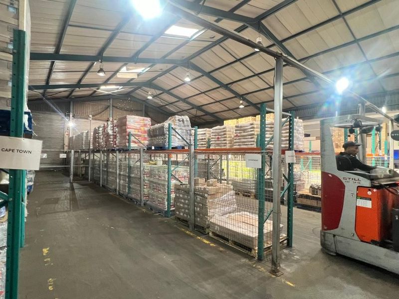 Spacious industrial warehouse facility featuring high-bay lighting, exposed steel roof trusses, and extensive heavy-duty steel racking systems for efficient storage and logistics operations.