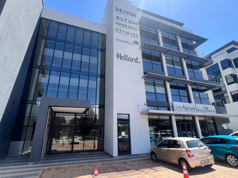Modern multi-story commercial office building featuring a glass facade, prominent corporate signage, and a paved entrance area.