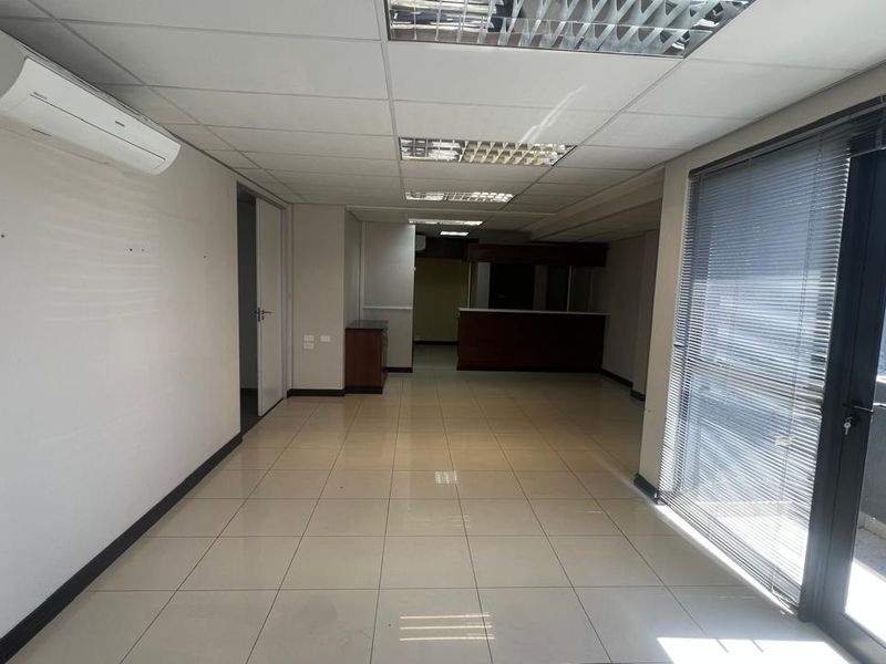 Spacious commercial office area featuring tiled flooring, suspended ceilings with recessed lighting, a built-in service counter, and a glass door leading to a balcony.