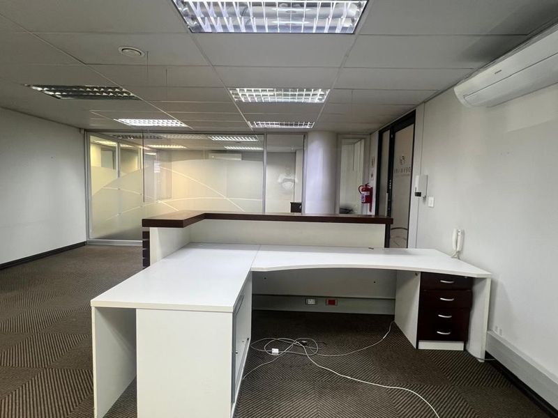 A vacant commercial office space featuring a built-in reception desk, glass partitioning, suspended ceilings, and a wall-mounted air conditioning unit.