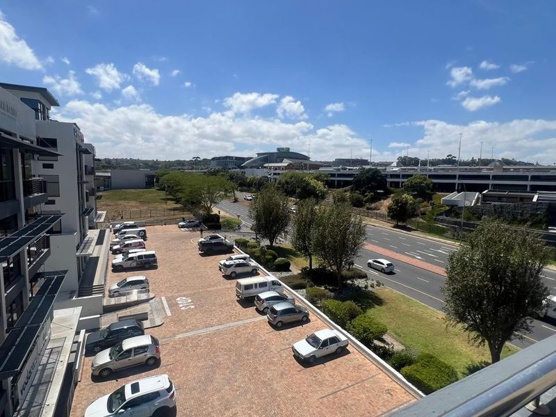 Elevated view overlooking a commercial parking area, adjacent office building facade, and surrounding urban infrastructure with clear sky.