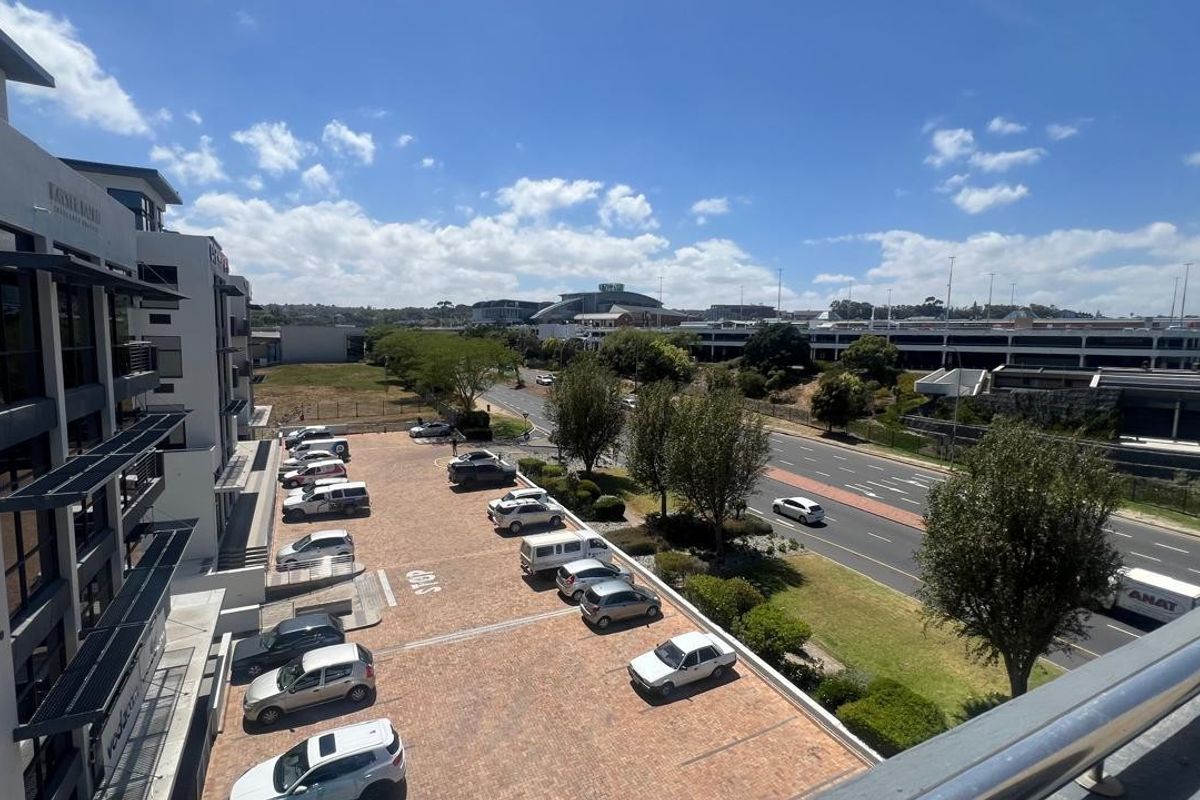 Elevated view overlooking a commercial parking area, adjacent office building facade, and surrounding urban infrastructure with clear sky.