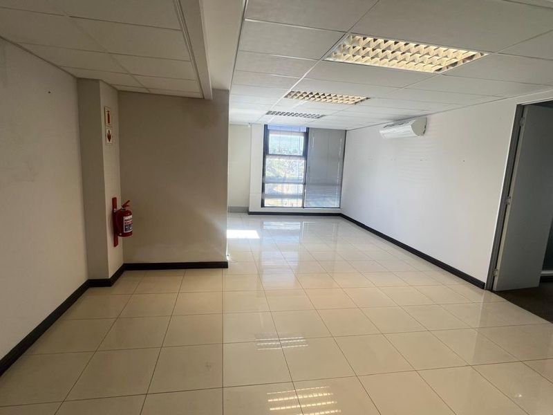 A bright, vacant commercial office space featuring polished ceramic floor tiles, a suspended ceiling with recessed lighting, and a wall-mounted air conditioning unit.