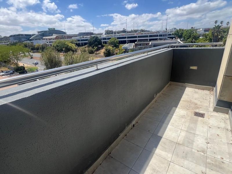 A balcony featuring tiled flooring and a stainless steel balustrade, offering an elevated view of the surrounding commercial area.
