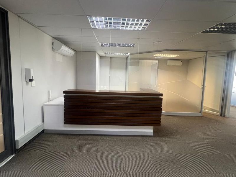 A professional commercial reception area featuring a built-in wooden desk, glass partitioning, suspended ceilings, and climate control, providing a clean and functional workspace entrance.