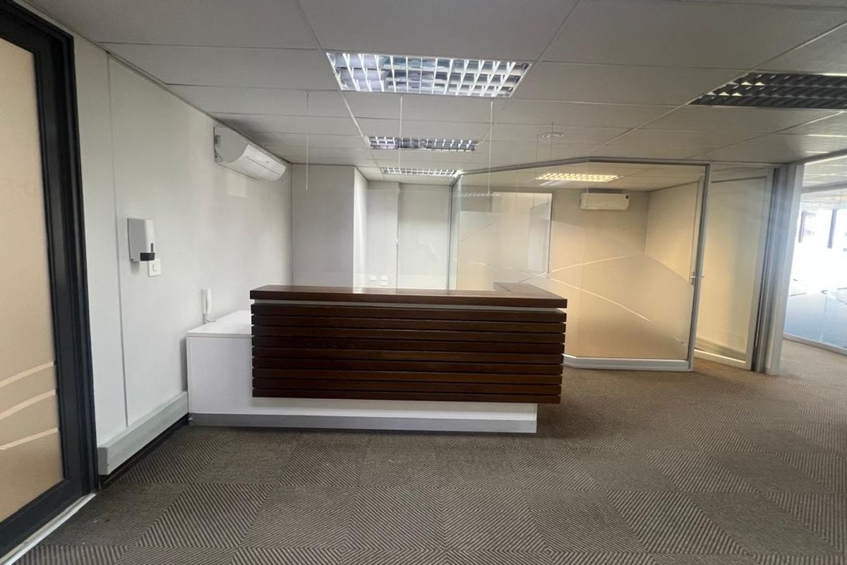 A professional commercial reception area featuring a built-in wooden desk, glass partitioning, suspended ceilings, and climate control, providing a clean and functional workspace entrance.