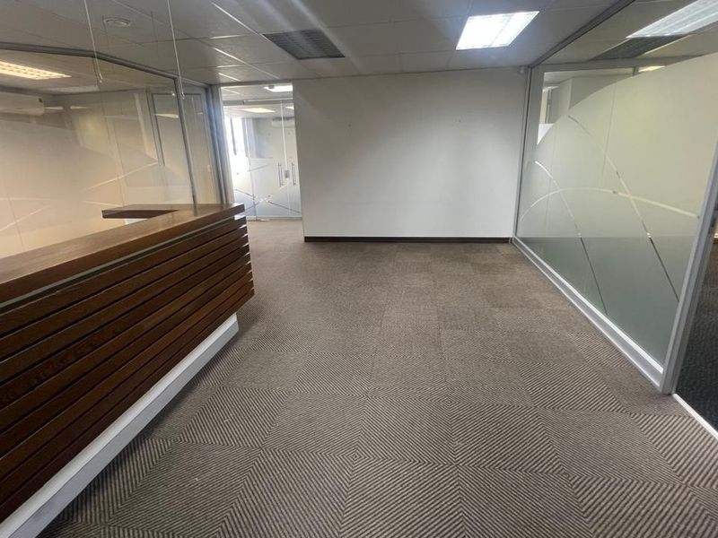 Empty commercial office space featuring a built-in wooden reception desk, glass partitions with privacy film, and carpeted flooring.
