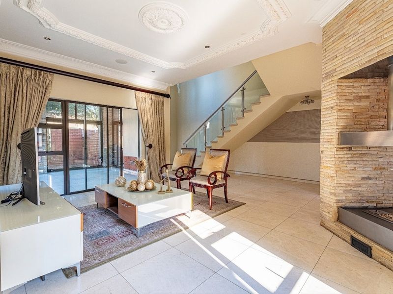 Spacious living room featuring a striking stone-clad fireplace, elegant ceiling detailing, and a modern staircase with a glass balustrade leading to the upper level.