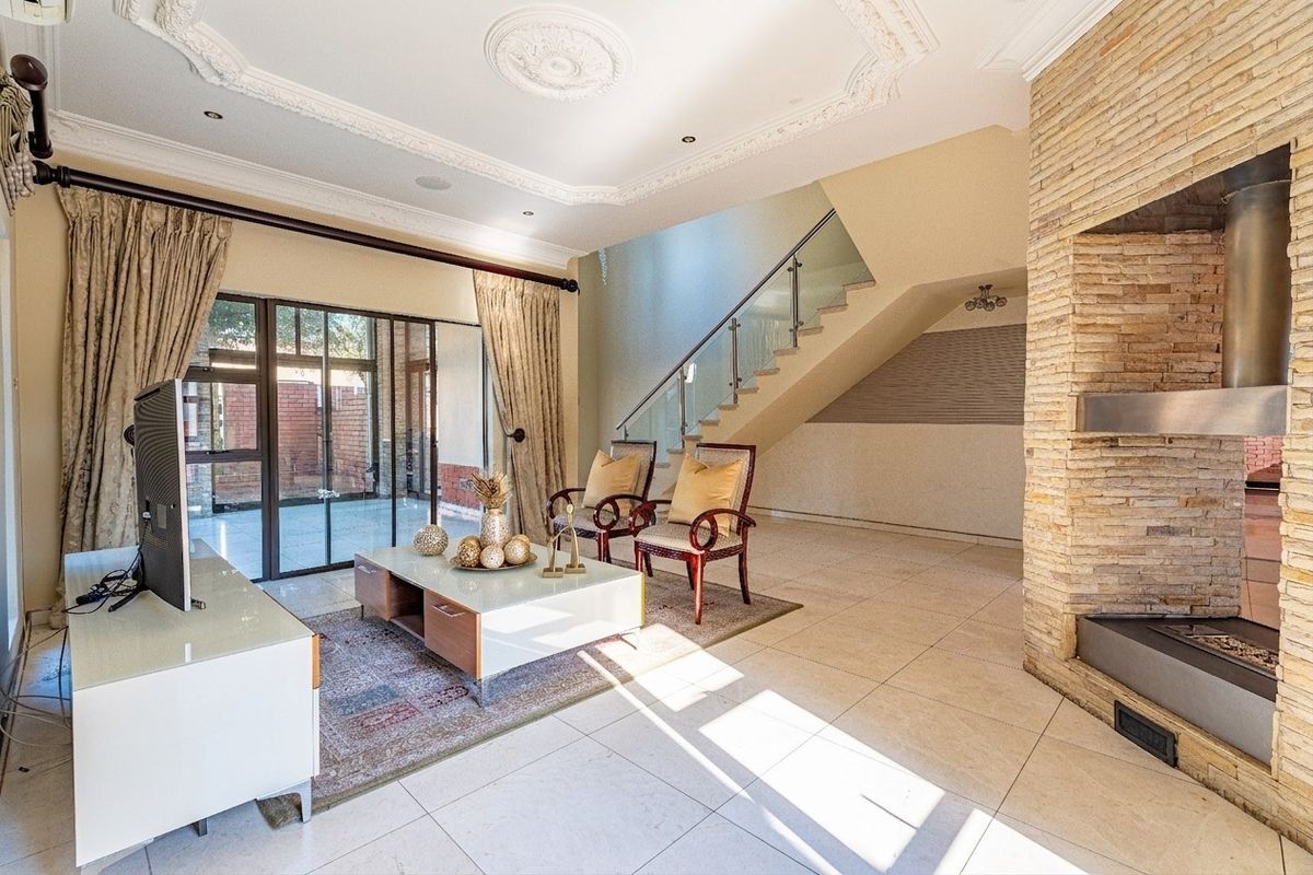 Spacious living room featuring a striking stone-clad fireplace, elegant ceiling detailing, and a modern staircase with a glass balustrade leading to the upper level.