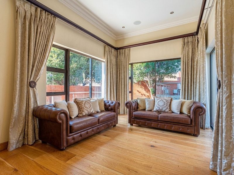 A bright and spacious living room featuring high-quality hardwood flooring, large windows with natural light, and elegant cornice detailing.