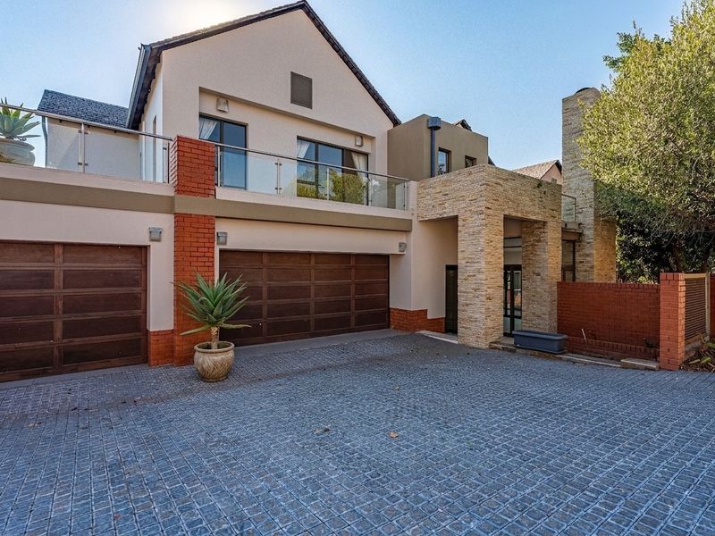 Modern double-storey residence featuring a paved driveway, double garage, stone-clad entrance, and an upper-level balcony with glass balustrades.
