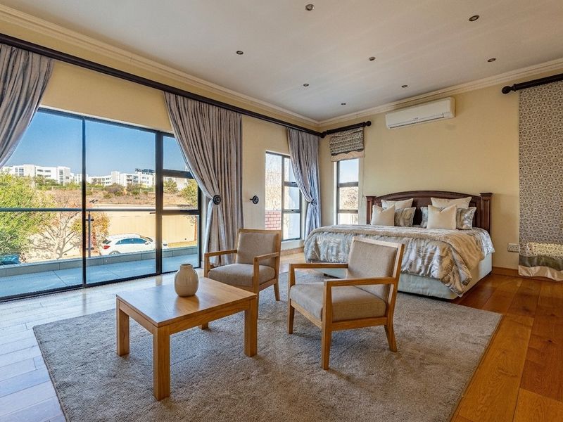 Spacious bedroom featuring hardwood flooring, recessed lighting, a wall-mounted air conditioner, and large sliding glass doors opening to a private balcony.