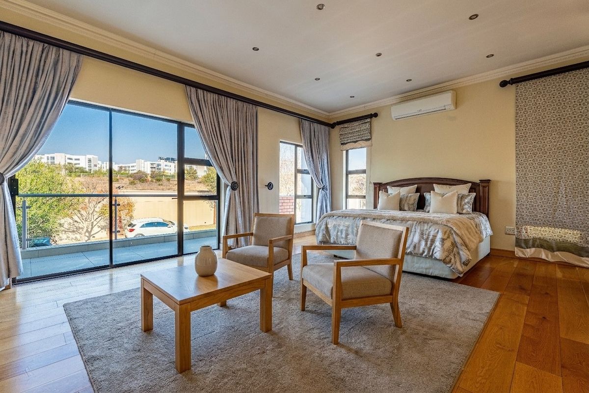 Spacious bedroom featuring hardwood flooring, recessed lighting, a wall-mounted air conditioner, and large sliding glass doors opening to a private balcony.