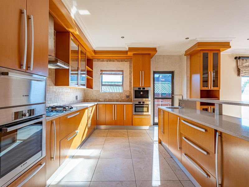 A spacious kitchen featuring light wood cabinetry, stone countertops, built-in appliances, and tiled flooring, offering a functional and well-lit workspace.
