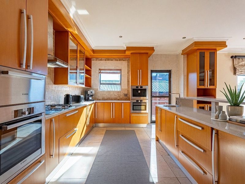A well-maintained kitchen featuring warm wood cabinetry, stone countertops, a central island, and integrated stainless steel appliances including an oven and microwave.