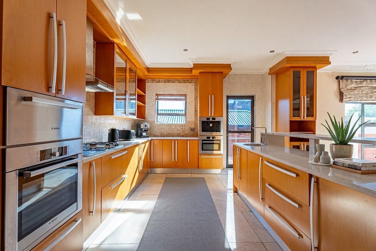 A well-maintained kitchen featuring warm wood cabinetry, stone countertops, a central island, and integrated stainless steel appliances including an oven and microwave.