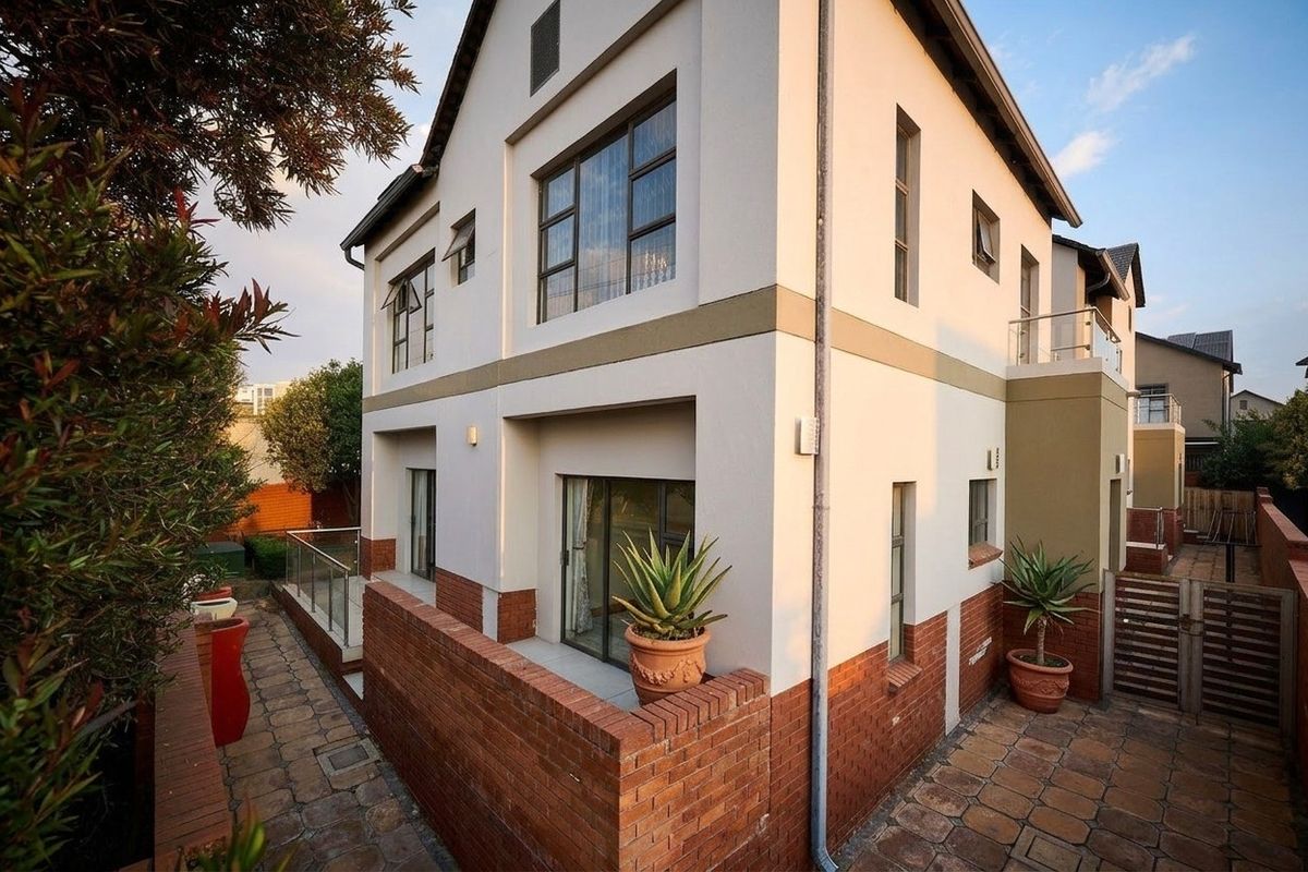 Rear view of a multi-story house featuring brick paving, a glass balustrade, and sliding door access to the outdoor area.