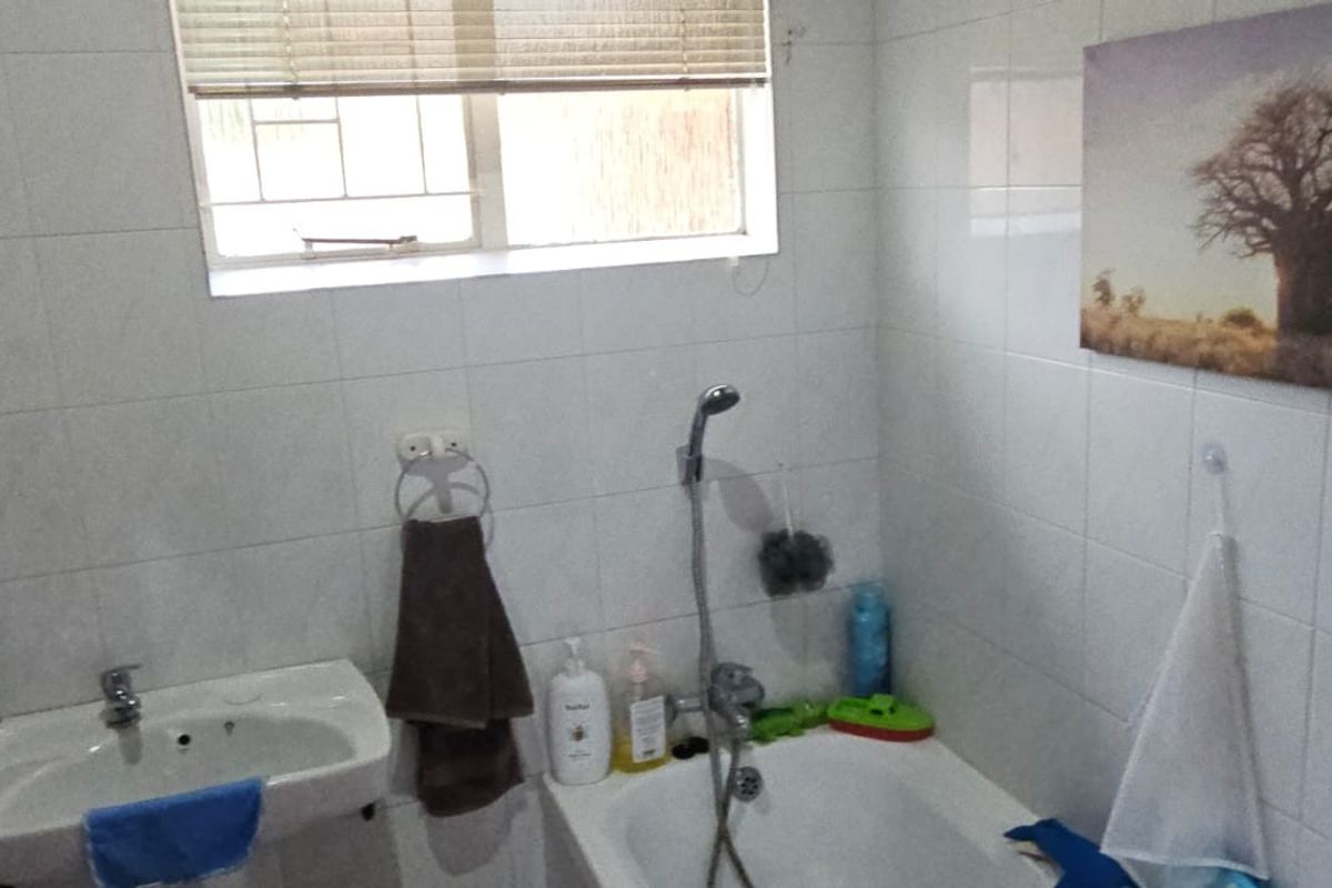 A functional bathroom featuring a wall-mounted basin, a bathtub with a handheld shower mixer, and tiled wall finishes.